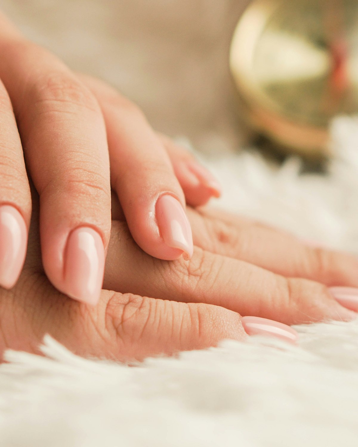 Bàn tay với bộ móng hồng nhạt tự nhiên trên nền lông mềm